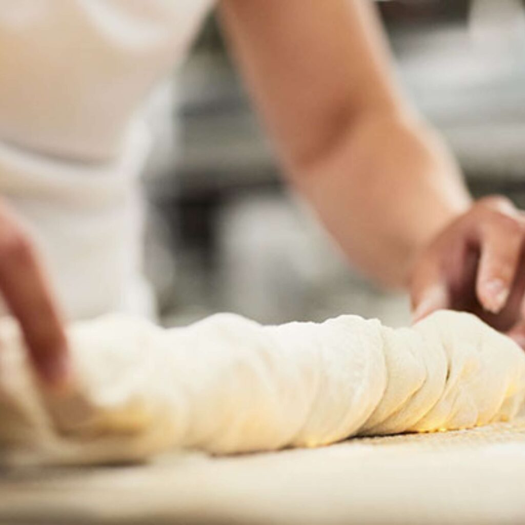 Ein Bäcker knetet den Teig und lässt ihn über einen längeren Zeitraum ruhen