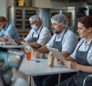 Viele Bäckerei-Mitarbeiter sitzen in einem Raum an Tischen und schauen sich auf ihren IPads E-learning Schulungen zu dem Thema Hygiene an.